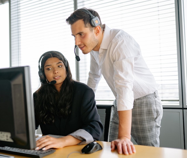 man and woman with headphones looking at computer